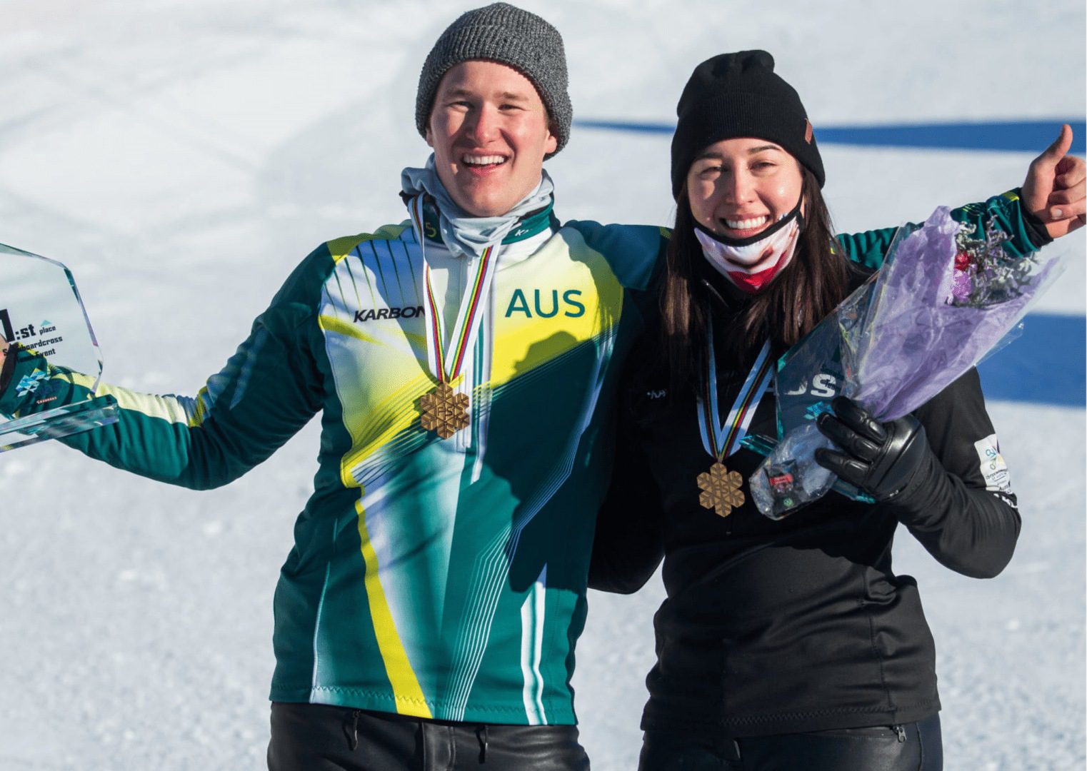 Two athletes holding gold medals and a trophy.